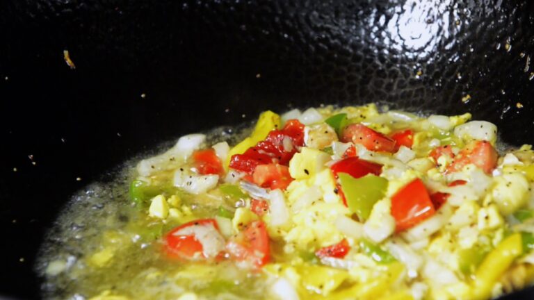 Ackee and saltfish cooking in a pan with onions and peppers