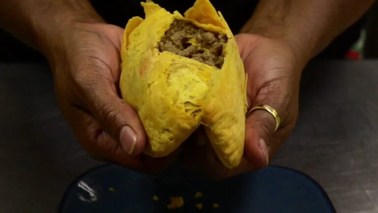 Hands holding a Jamaican beef patty broken open to show the seasoned beef filling inside the golden crust